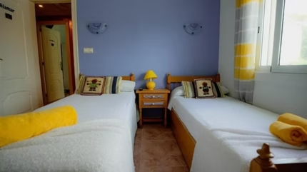 Habitacion con recamaras dobles almohadones tejidos y lampara amarilla