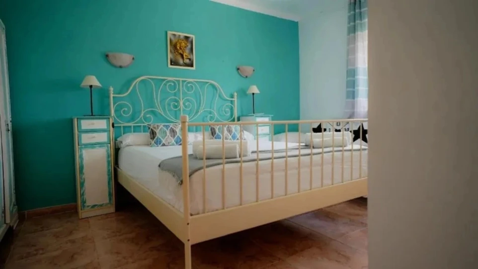 Vista inclinada de cama y almohadones blancos con fondo de pared azul claro