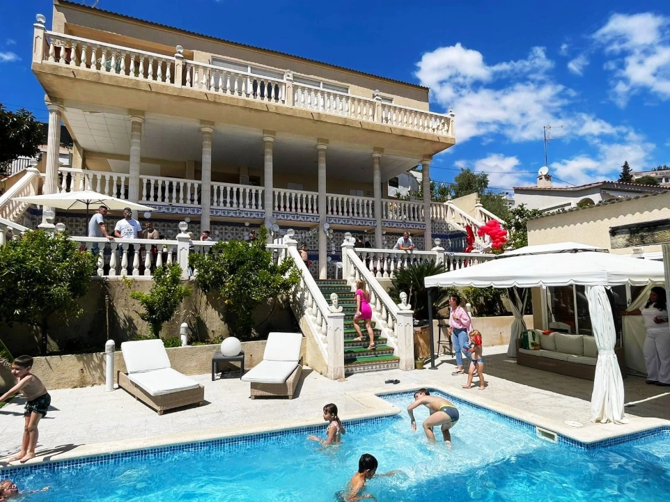 Piscina llena de niños y vista de villa